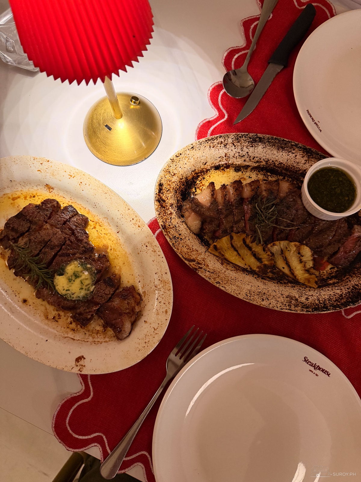 Two steak platters seen from above, one topped with herb butter and one with grilled pineapple and chimichurri, at The Steakhouse by Carne & Deli in Cebu
