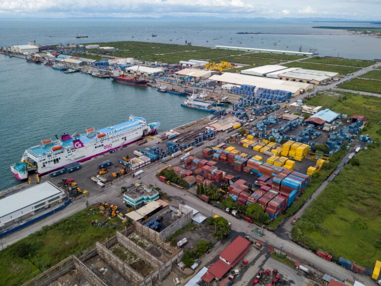 A 2GO Travel ferry in magenta and blue livery berthed at BREDCO Port in Bacolod, its stern ramp down beside stacks of 2GO containers and forklifts on the apron