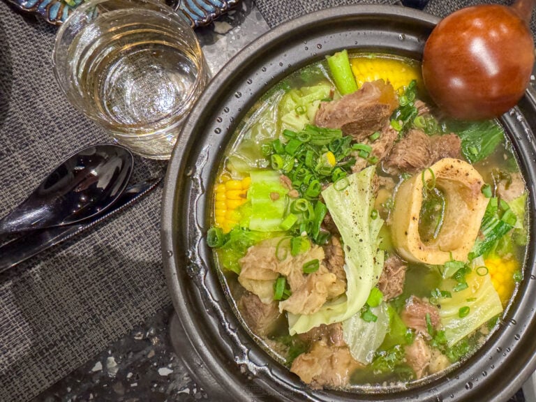 Bulalo in a dark clay pot at 7107 Restaurant Cebu City, with a ring of bone marrow at the center, sweet corn, cabbage and spring onions in a clear beef broth