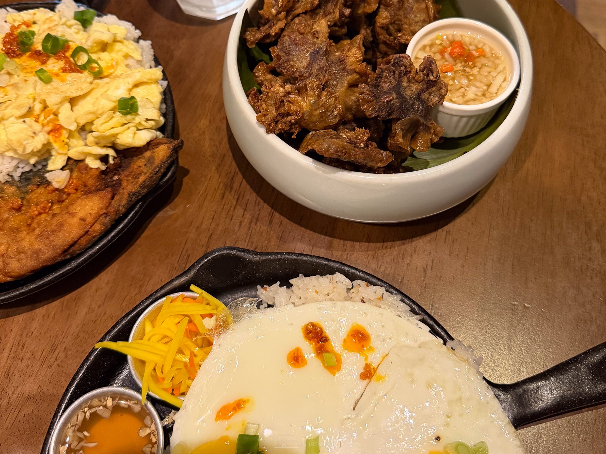 Three sizzling brunch plates at Balai with fried fish, scrambled egg, crisp fried meat and a fried egg over rice