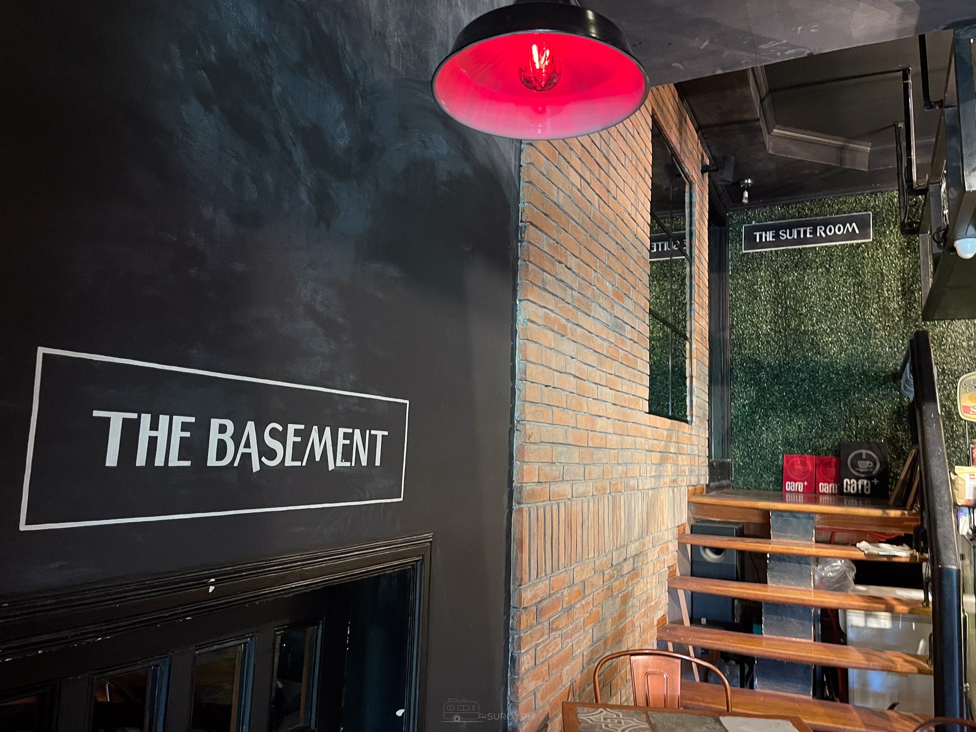 Signs at Balai reading The Basement and The Suite Room beside brick wall and a red pendant lamp