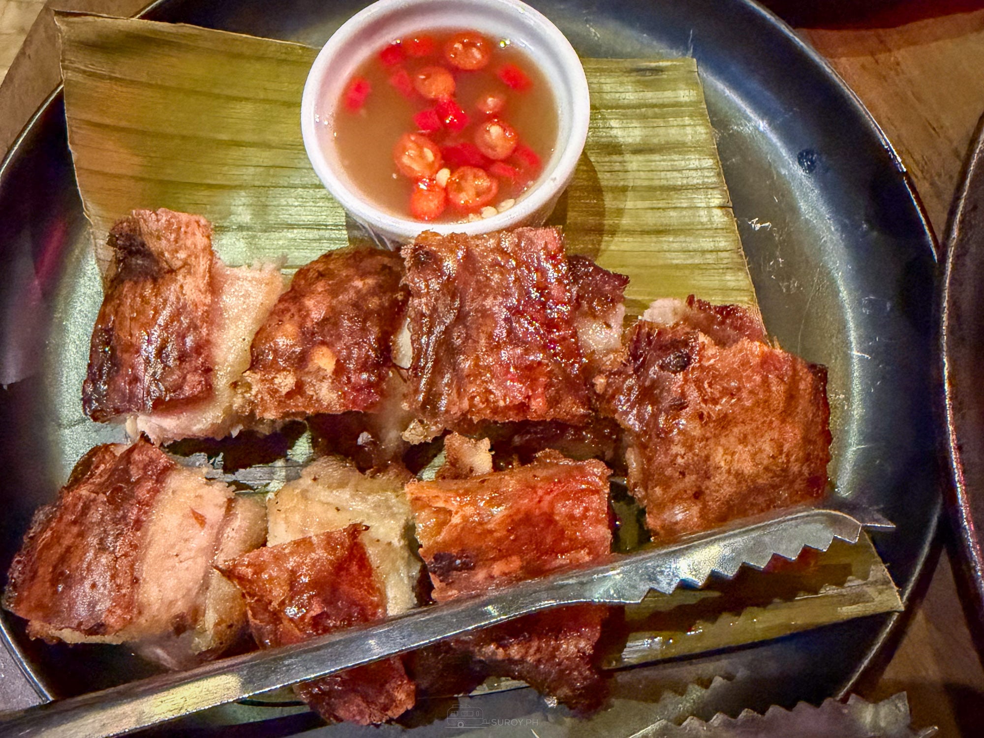 Charcoal grilled pork belly chopped on banana leaf at Balai served with chili vinegar and tongs