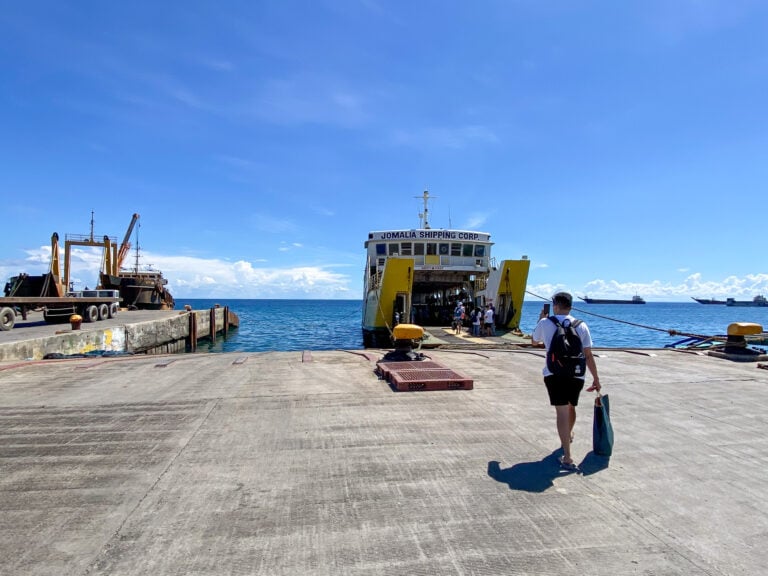 Passenger walking along the Consuelo pier toward a yellow Jomalia Shipping ferry with its bow ramp down and people boarding