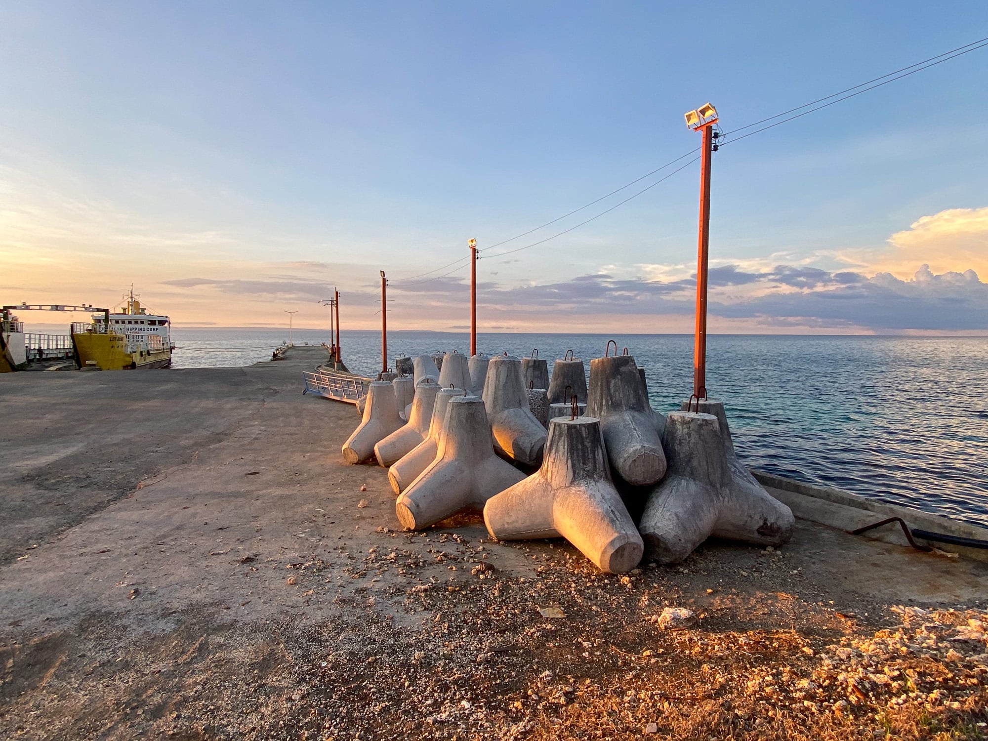 Concrete tetrapods stacked along the Consuelo pier on Camotes with a ferry moored alongside and flat sea at sunset