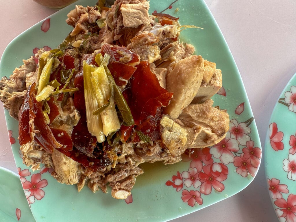 Chopped Carcar lechon on a plate with lengths of lemongrass from the cavity stuffing visible in the pile