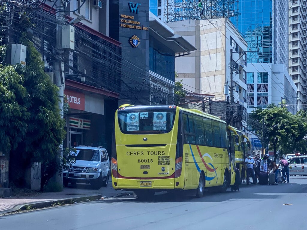 A yellow Ceres Tours coach parked on a Cebu City street while passengers load luggage at the door