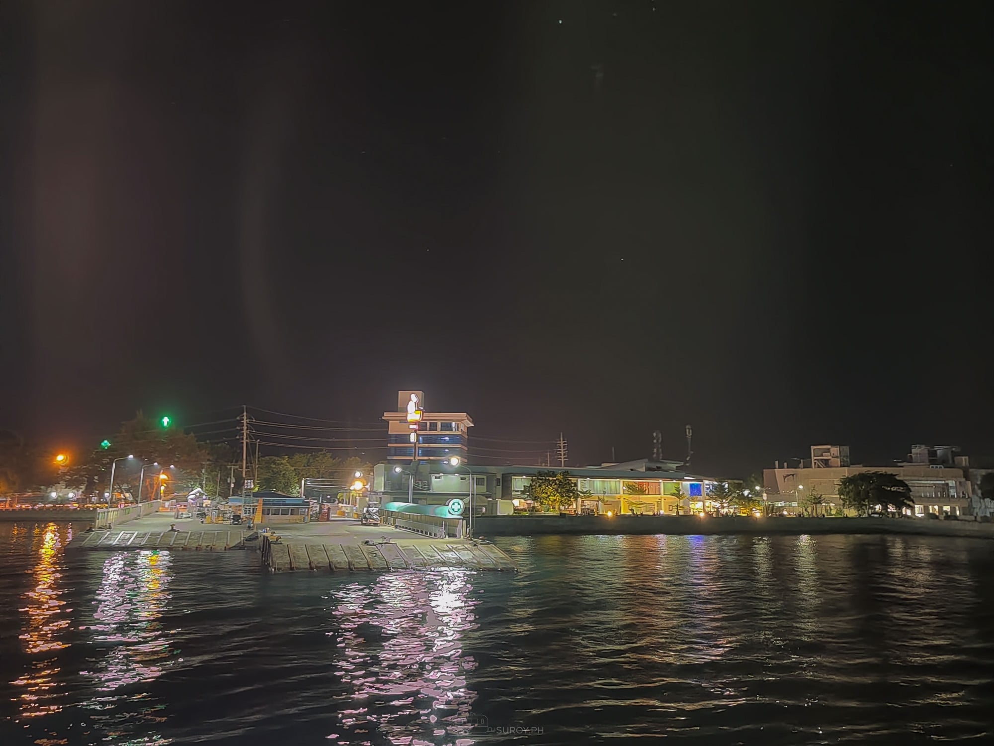 Night view across the water toward the lit Danao waterfront with a ferry alongside the pier