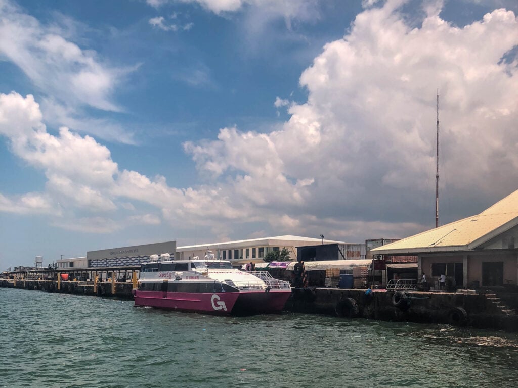 A magenta SuperCat fast craft in 2GO livery berthed alongside the terminal shed at BREDCO Port under a bright sky