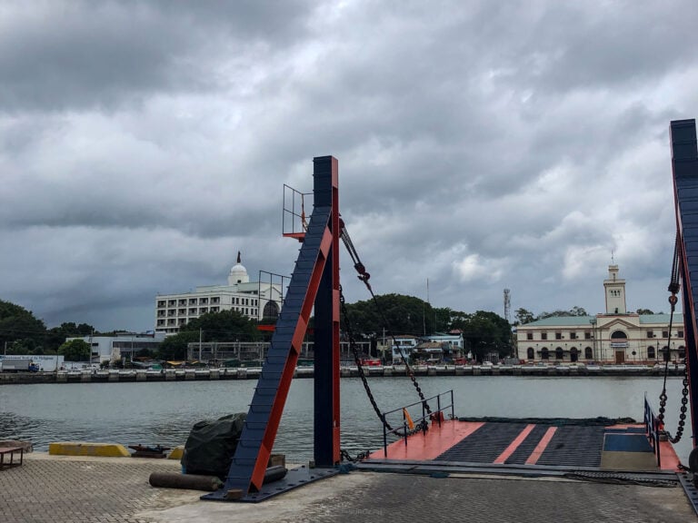 A roll-on roll-off ramp and its gantries on a wharf under a heavy grey sky, the Iloilo Customs House across the water