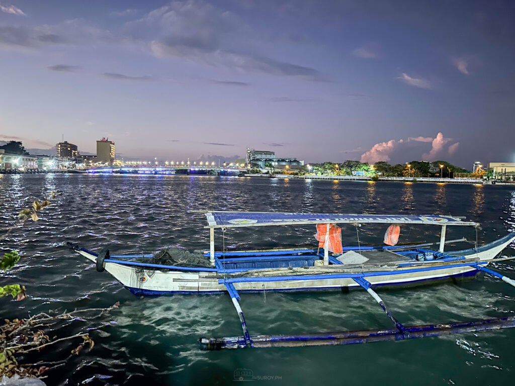 Outrigger bancas moored in the shallows at dusk with the lights of the Iloilo waterfront strung out behind them