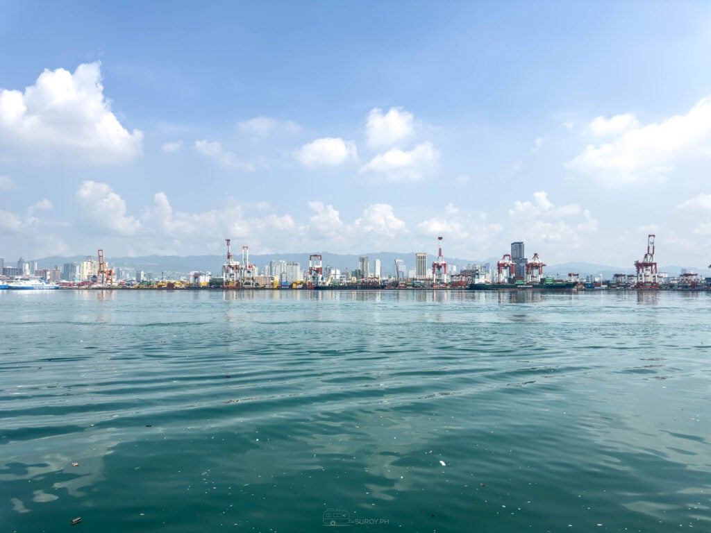 The Port of Cebu container berths and gantry cranes seen low from the water, with the city skyline and hills behind