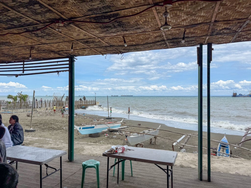 Tables under a nipa roof at Talisay Litson Food Park looking out to the beach and the open sea
