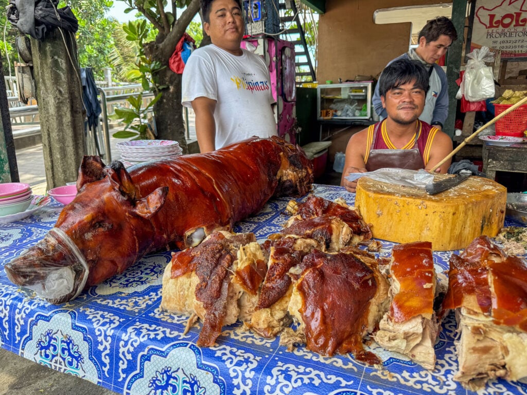 A whole roast pig on a stall counter at Talisay Litson Food Park with slabs of lechon laid out in front