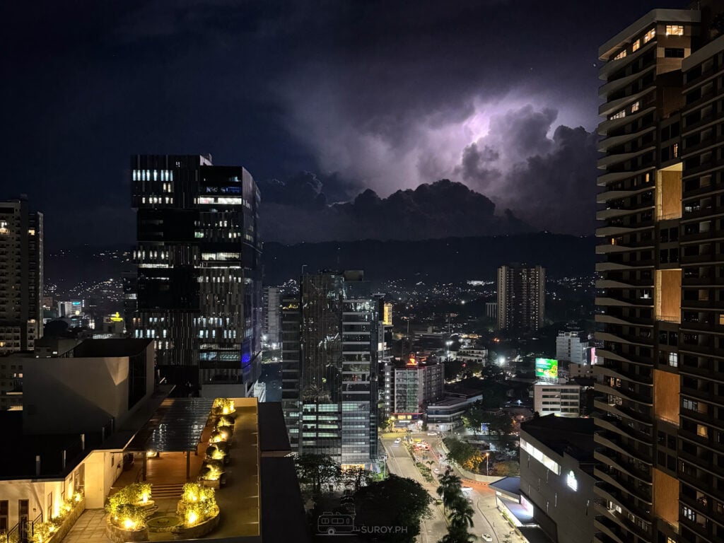 Lightning behind the Cebu skyline at night, seen from a high balcony with a purple storm cloud above the lit buildings
