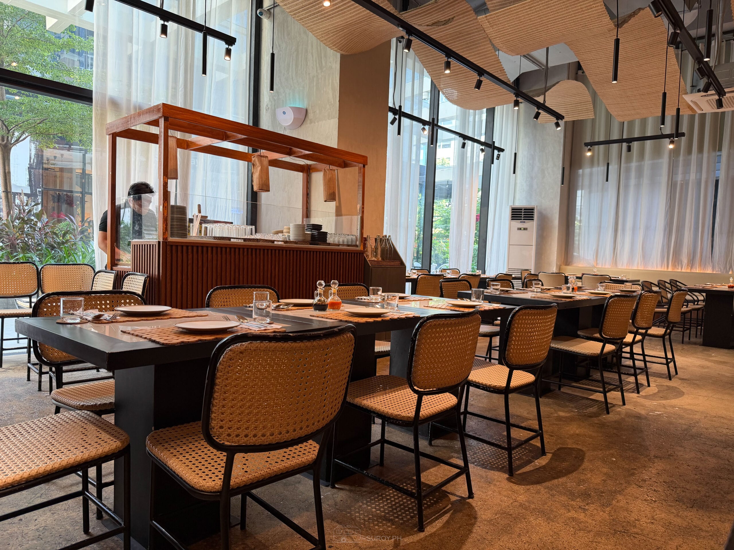 Dining room at ATO-AH with rattan chairs, dark tables and a high ceiling