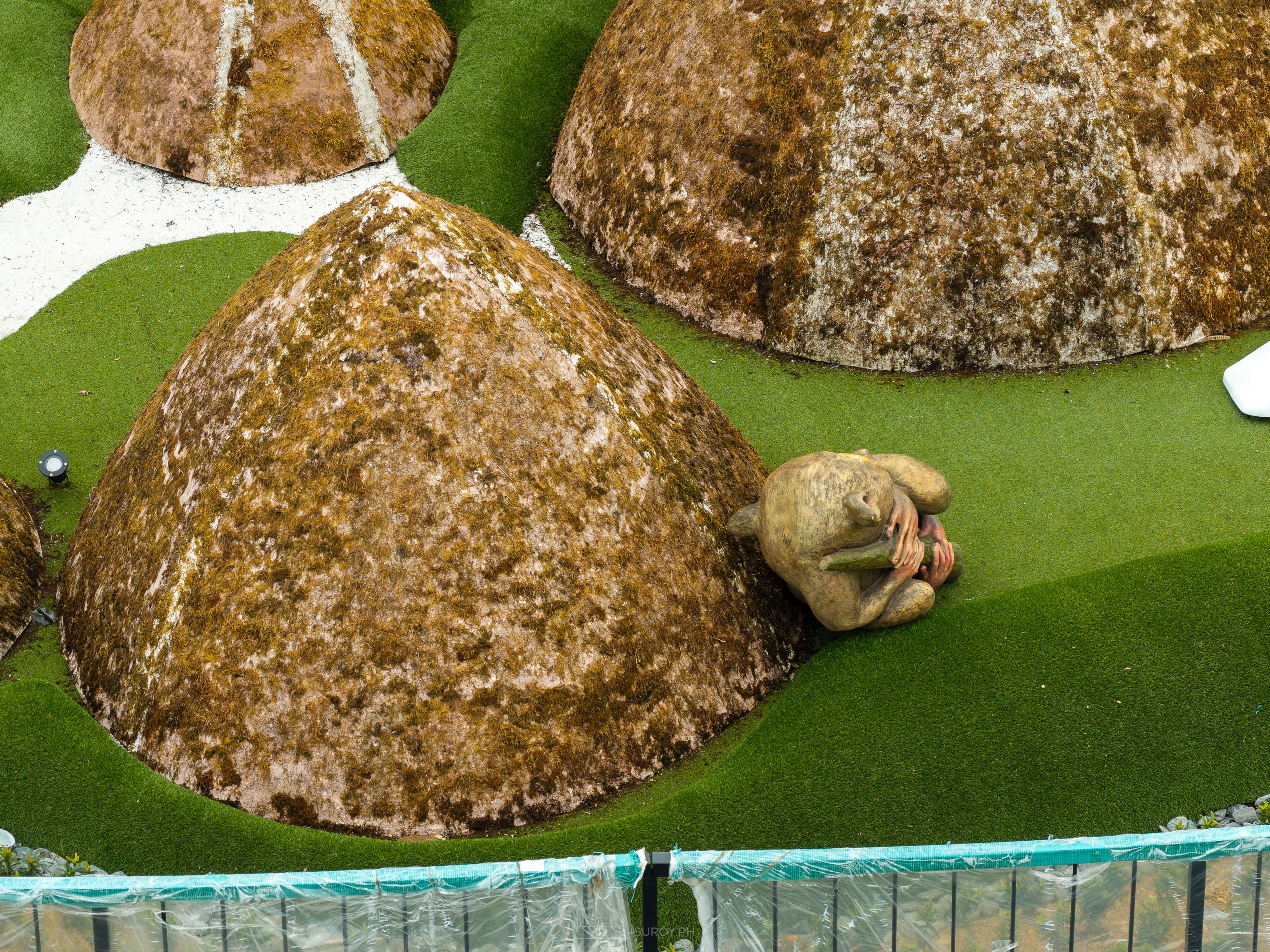 Close aerial of brown cone-shaped mounds modeled on the Chocolate Hills on a mini golf green, with a small tarsier figure beside the largest mound