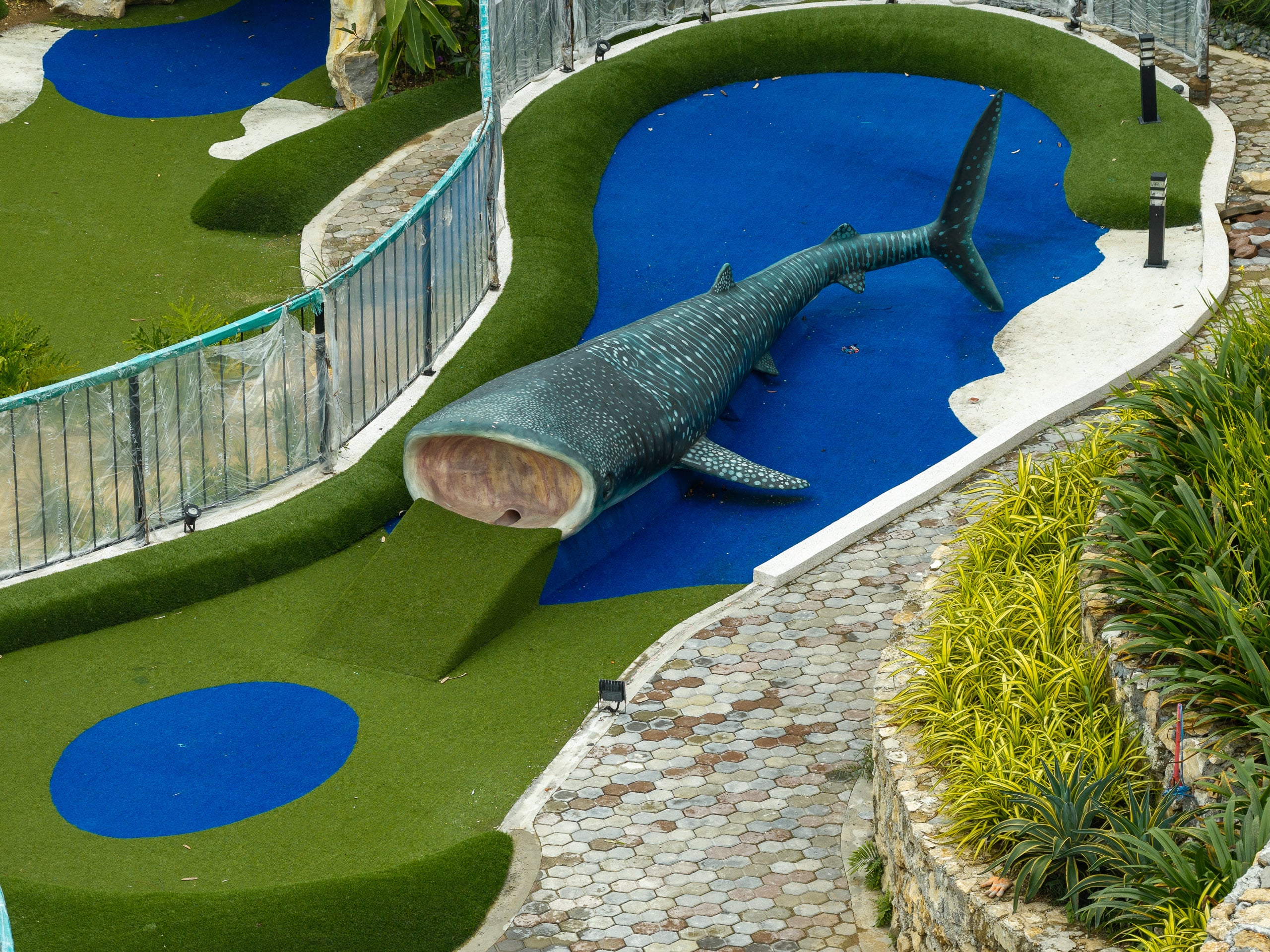 Whale shark sculpture rising from a pond of blue artificial turf beside a mini golf fairway