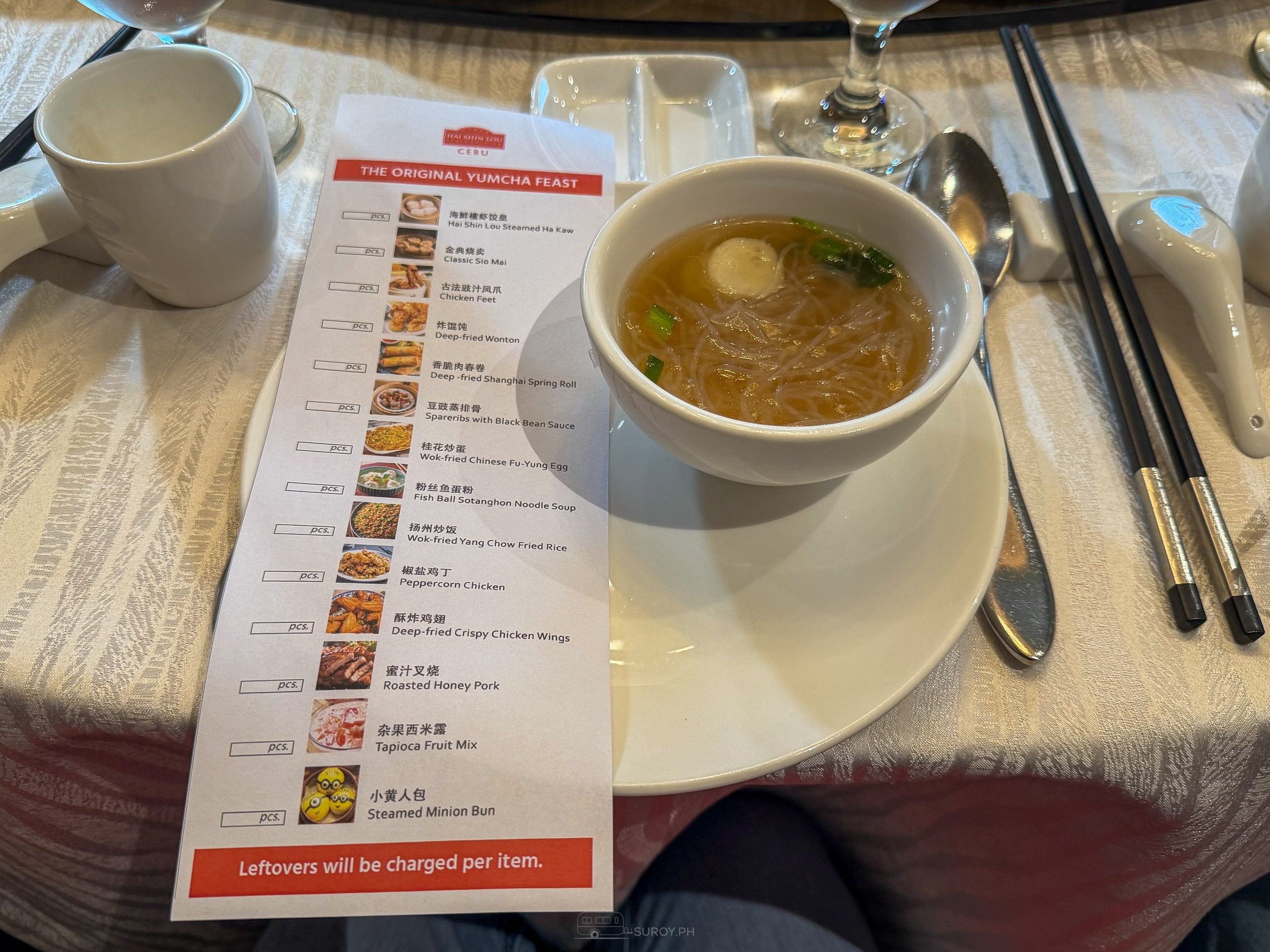 The Original Yum Cha Feast order sheet on a white tablecloth, a box marked pcs beside each dish, next to a bowl of fish ball noodle soup