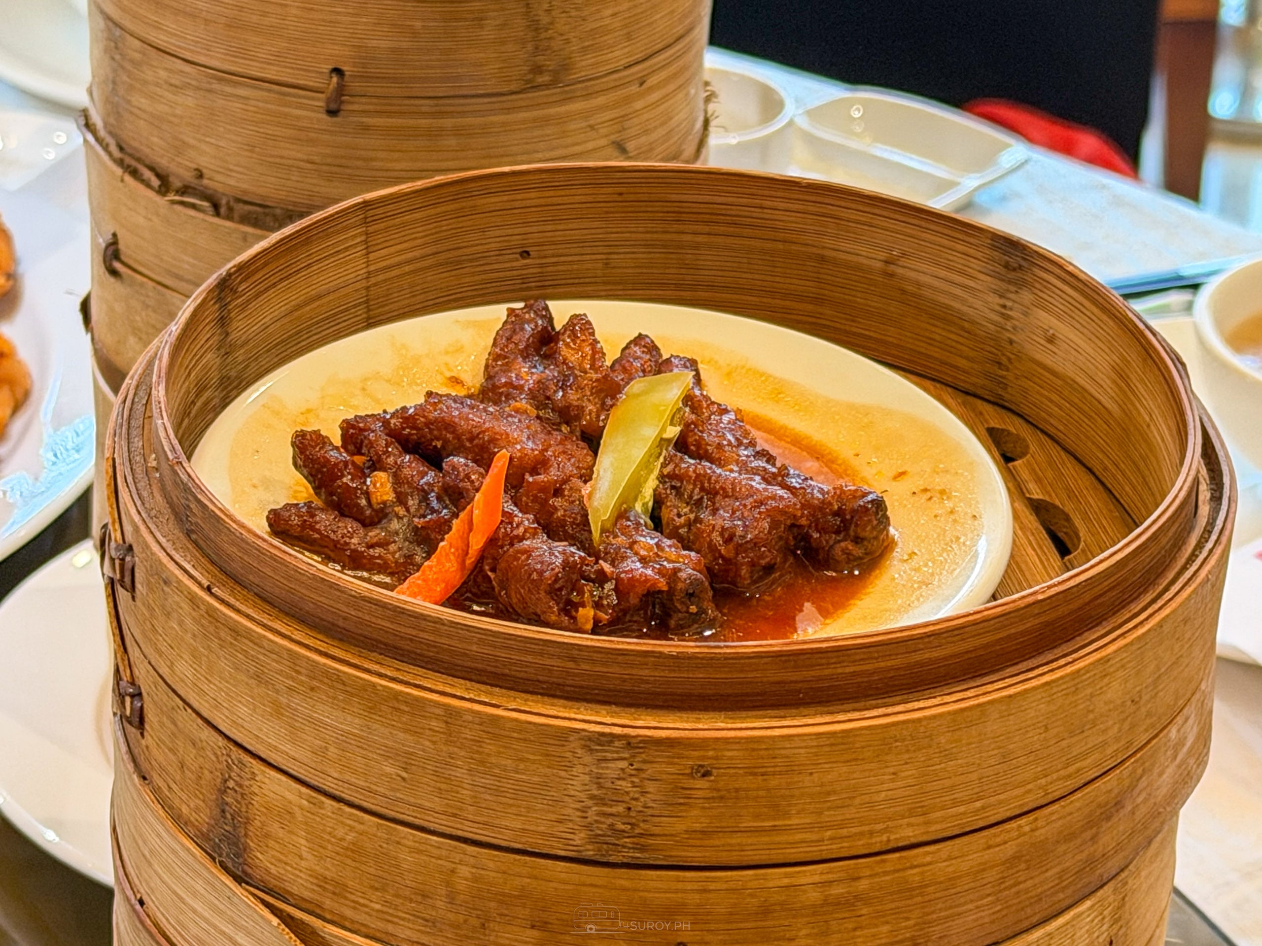 Chicken feet in a dark red black bean glaze in a bamboo steamer, with a slice of chili and carrot