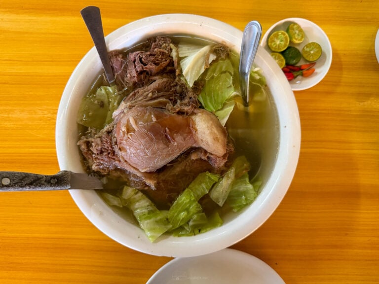 A bowl of Cebu pochero at Marjo's with a whole beef shank, clear broth and cabbage, beside a saucer of calamansi and red chili