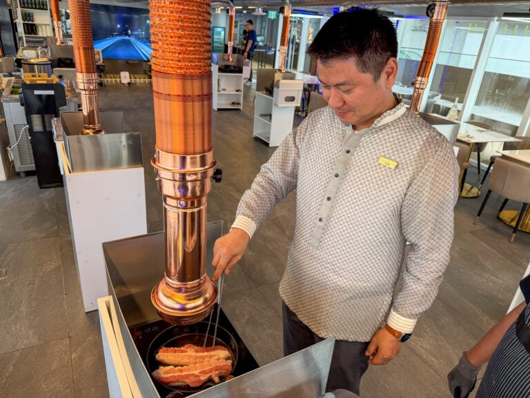 A staff member at Seoul Moon in Astra Lifestyle Centre, Mandaue, cooking strips of pork belly in a round pan at a stainless grill station under a copper exhaust hood