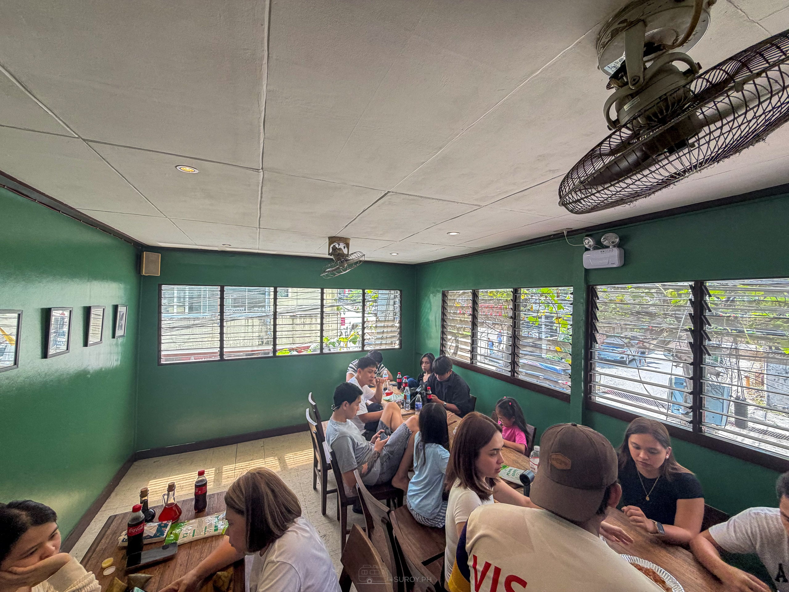 Full dining room at Tatang's with green walls, louvered windows, a wall fan and diners at long tables
