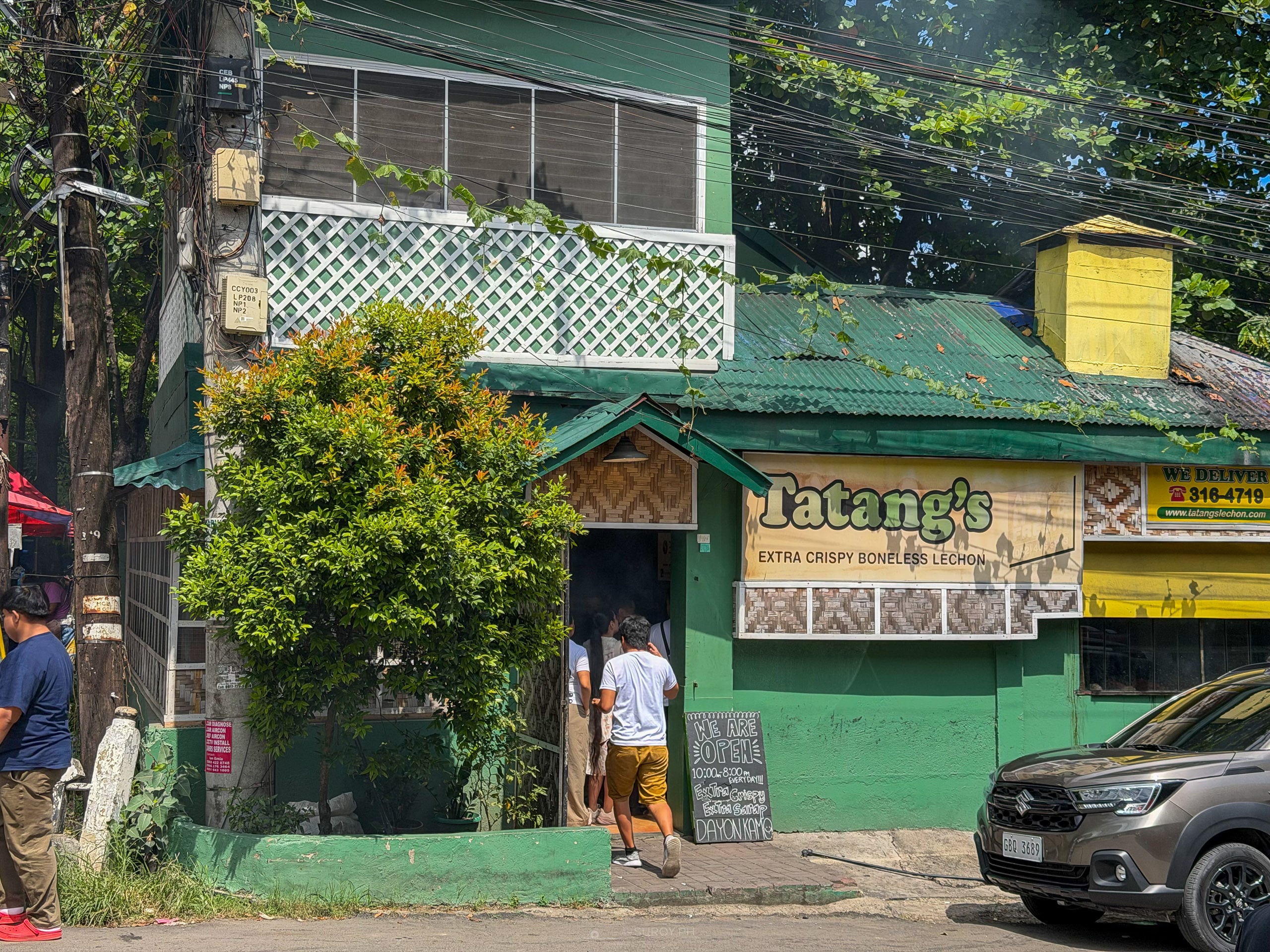 Green two-story house on Wilson Street with the Tatang's sign, a chalkboard reading we are open 10 AM to 8 PM every day, and diners walking in at the door