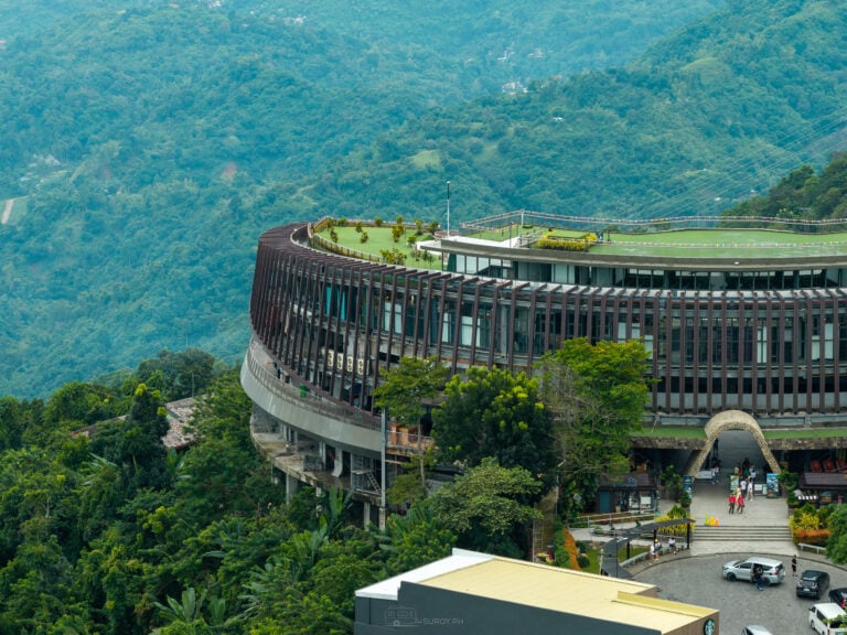 Aerial of The Circle at Tops in Busay, a round five-story building with a turf roof and an arched entrance, forested mountains behind